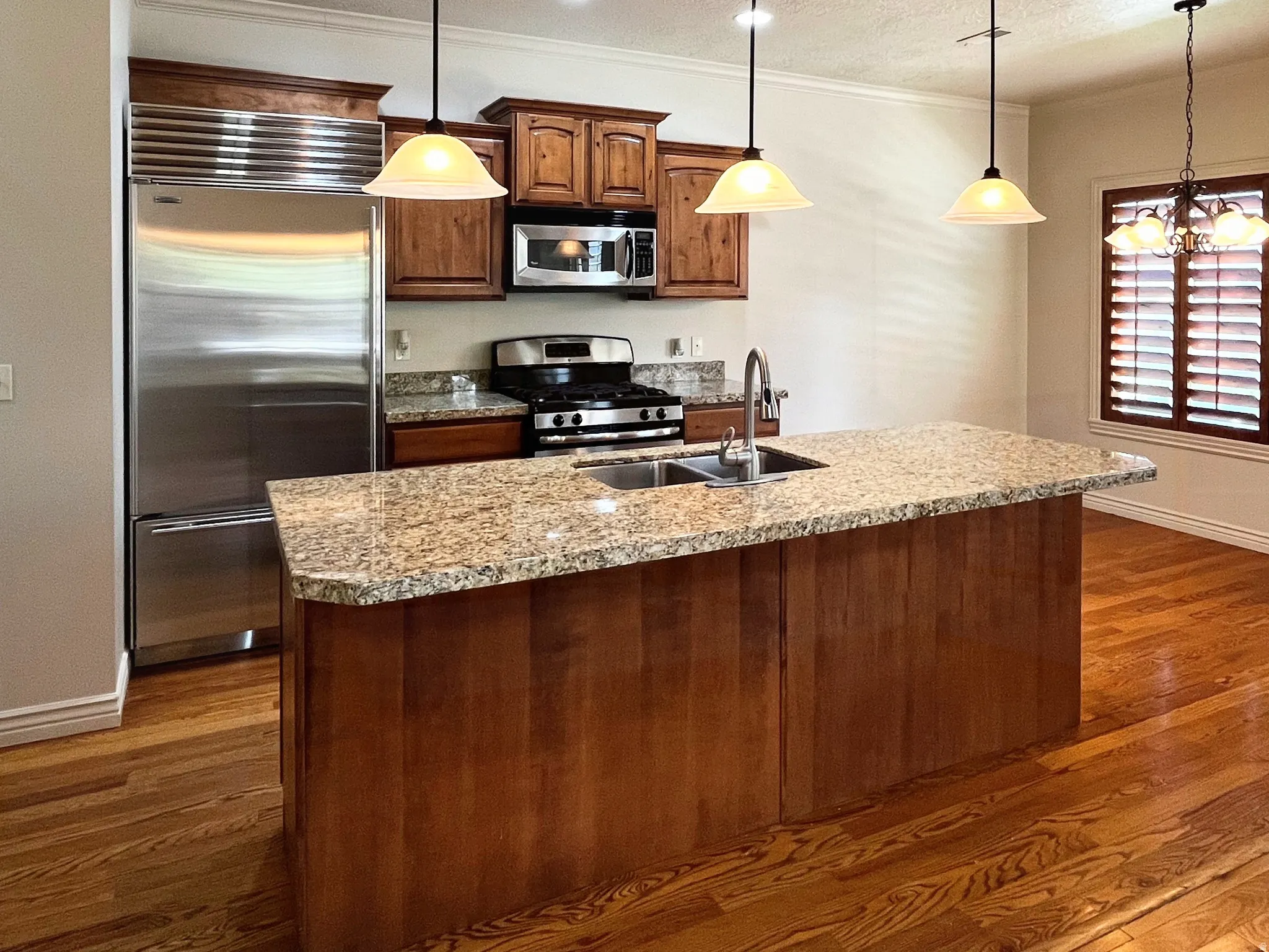 Kitchen featuring stainless steel appliances, light stone countertops, an island with sink, dark wood-type flooring, and ornamental molding