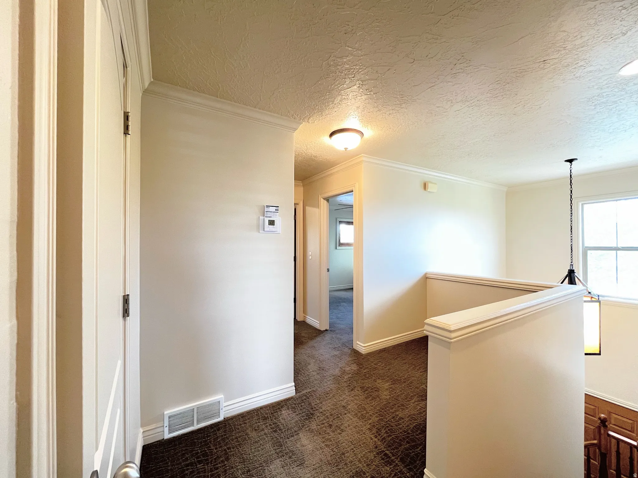 Hallway featuring an upstairs landing, dark carpet, ornamental molding, and a textured ceiling
