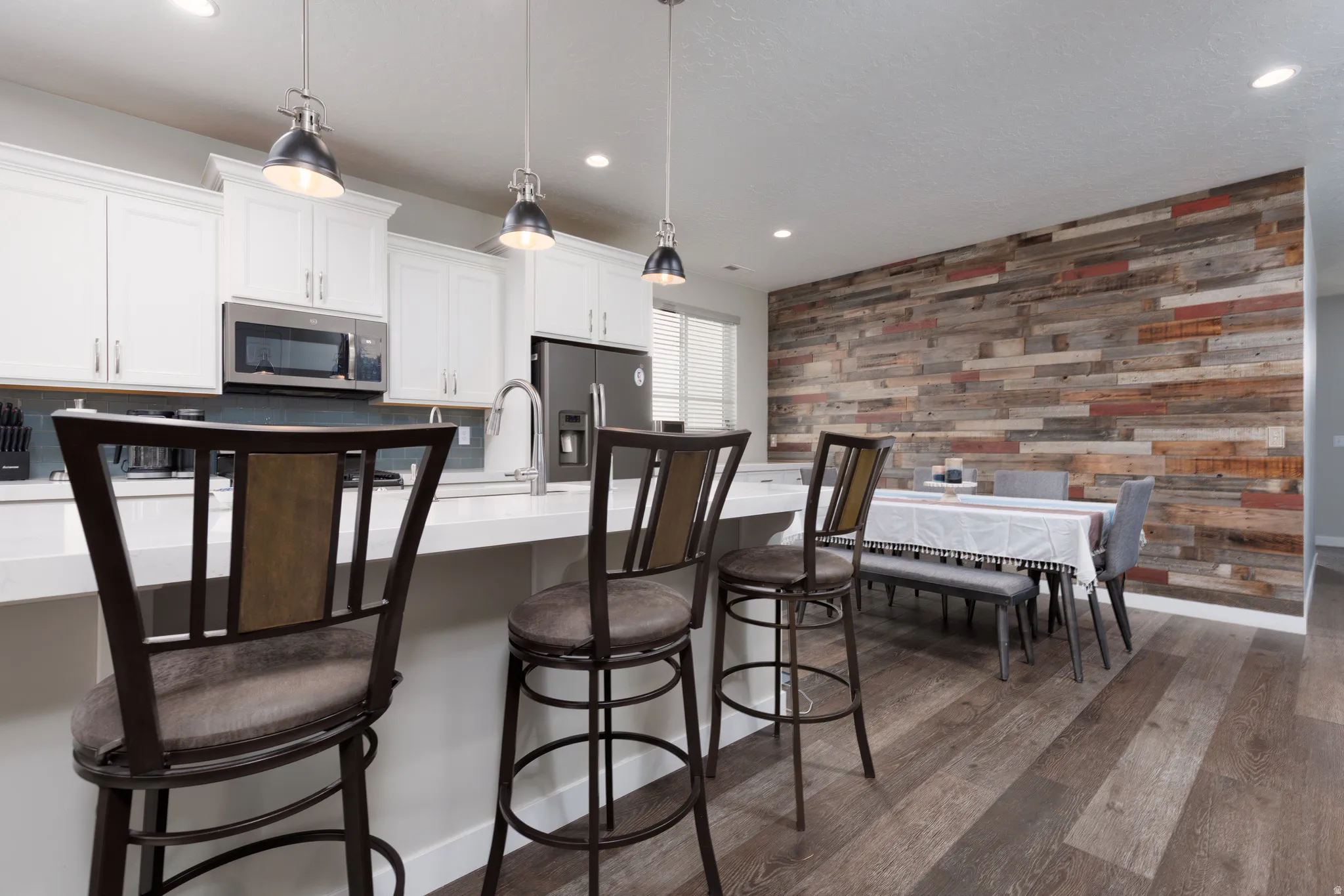 Kitchen featuring white cabinetry, appliances with stainless steel finishes, hanging light fixtures, distressed wood wall, breakfast bar stools and dark wood-style flooring