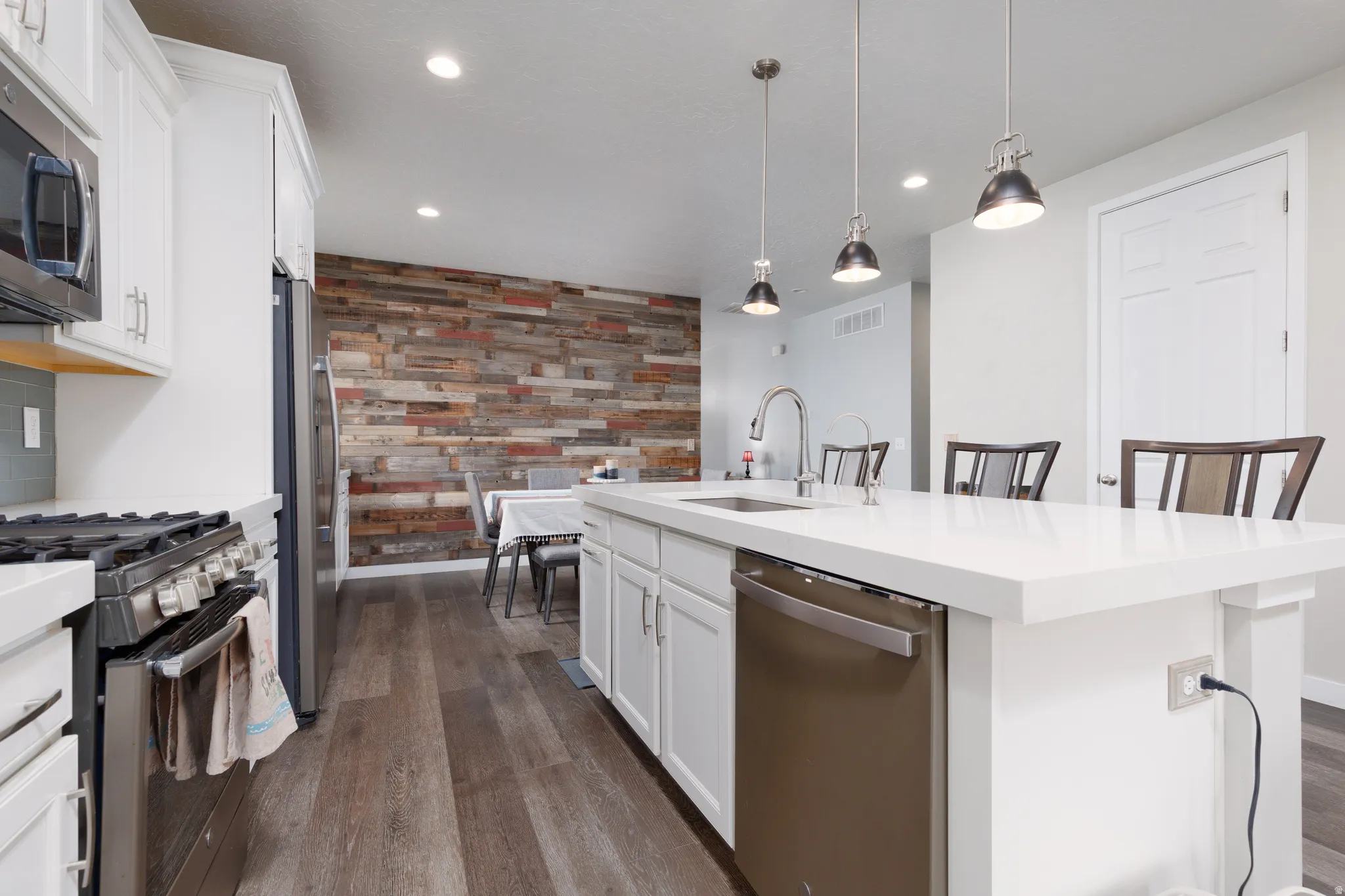 Kitchen with barn wood accent wall, white cabinets, stainless steel appliances, a breakfast bar, hanging light fixtures and custom countertops.