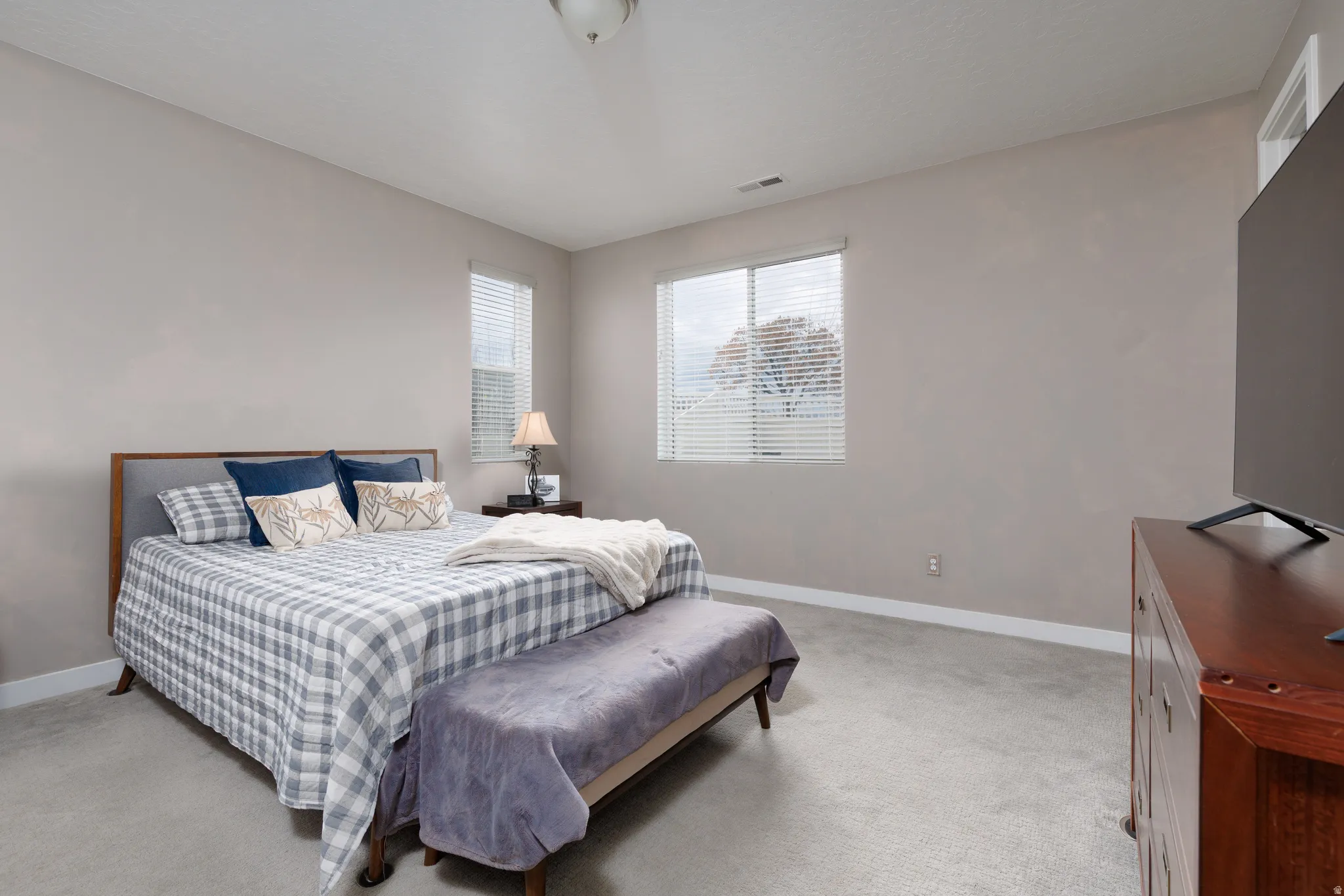 Master bedroom featuring light carpet, custom blinds and ample natural lighting.