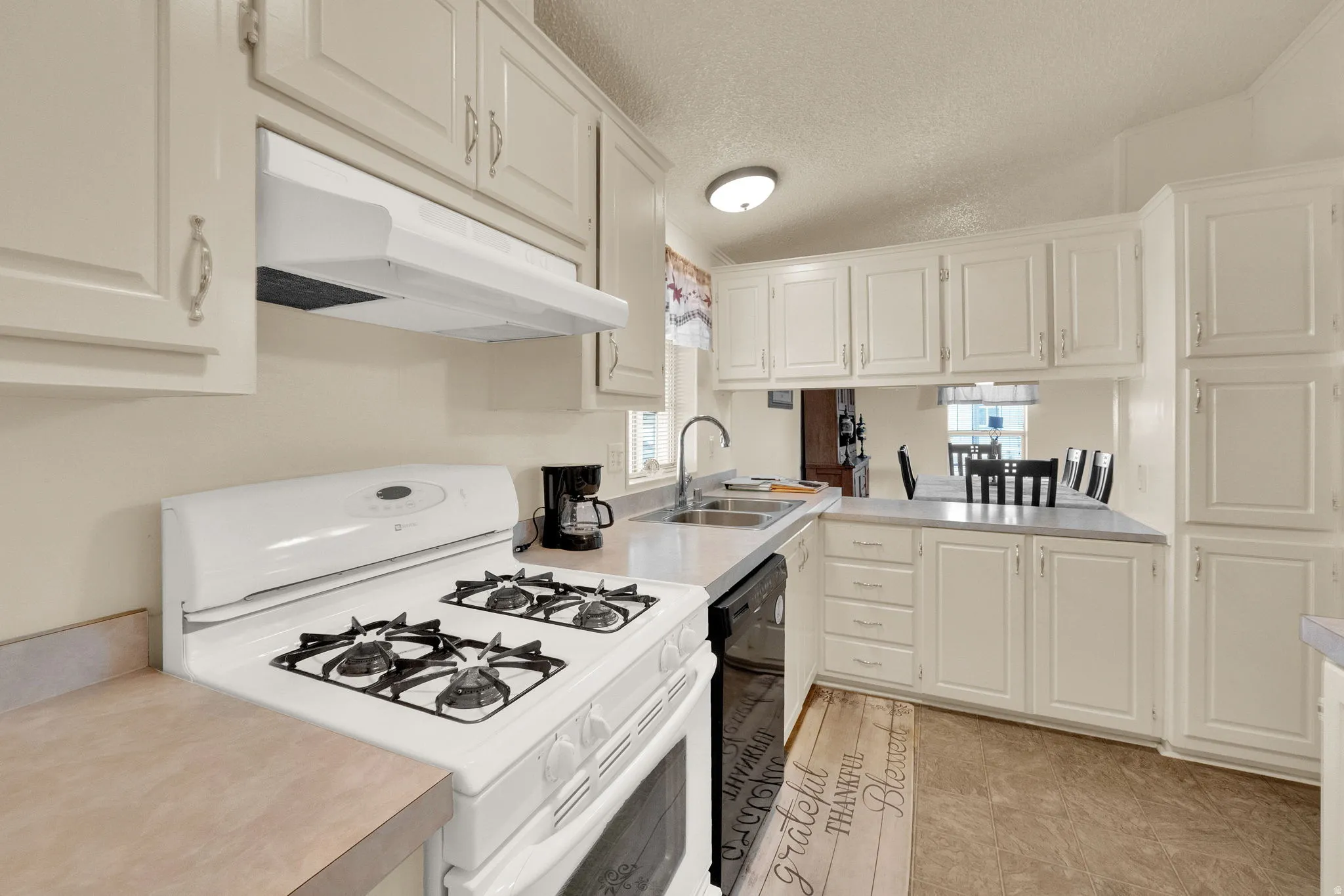 Kitchen with white gas range oven, under cabinet range hood, a textured ceiling, light countertops, and white cabinetry