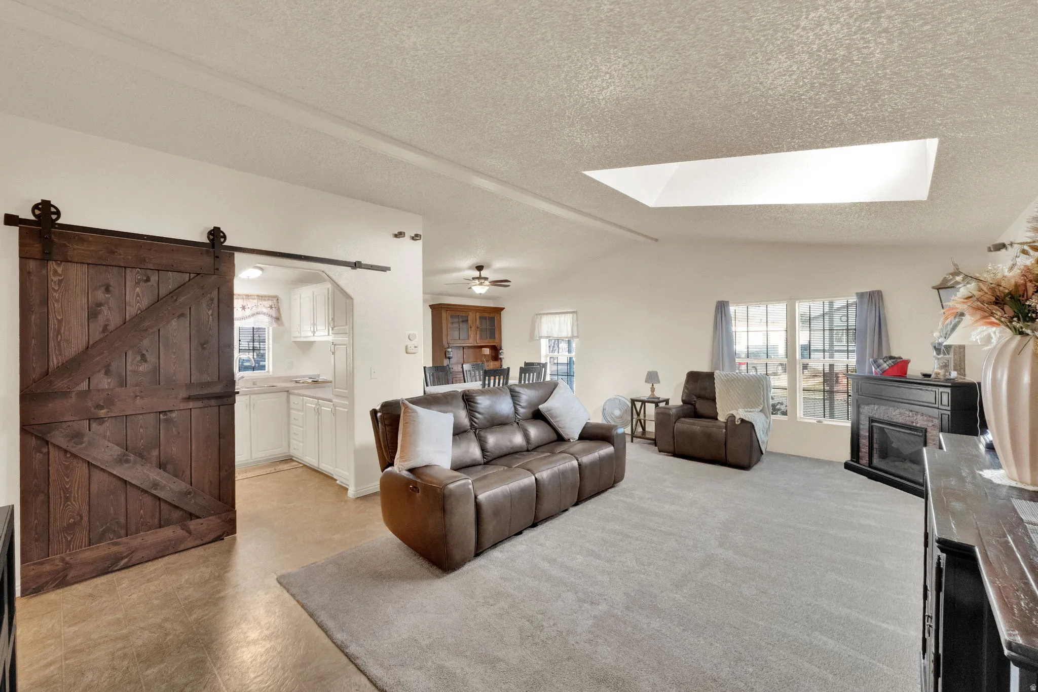 Living area featuring lofted ceiling, a textured ceiling, a glass covered fireplace, light floors, and a ceiling fan
