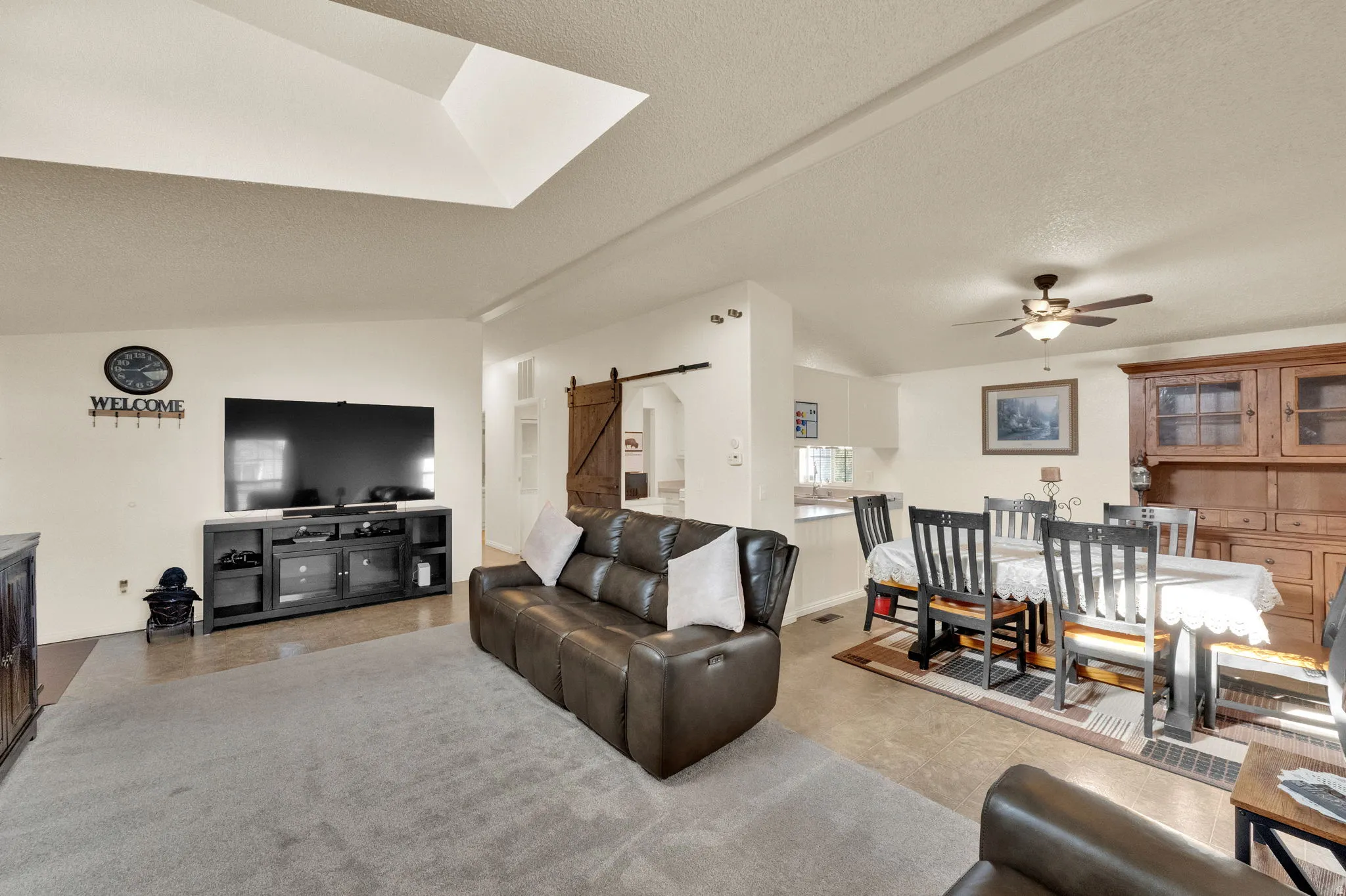 Living room with a barn door, a textured ceiling, lofted ceiling, and a ceiling fan