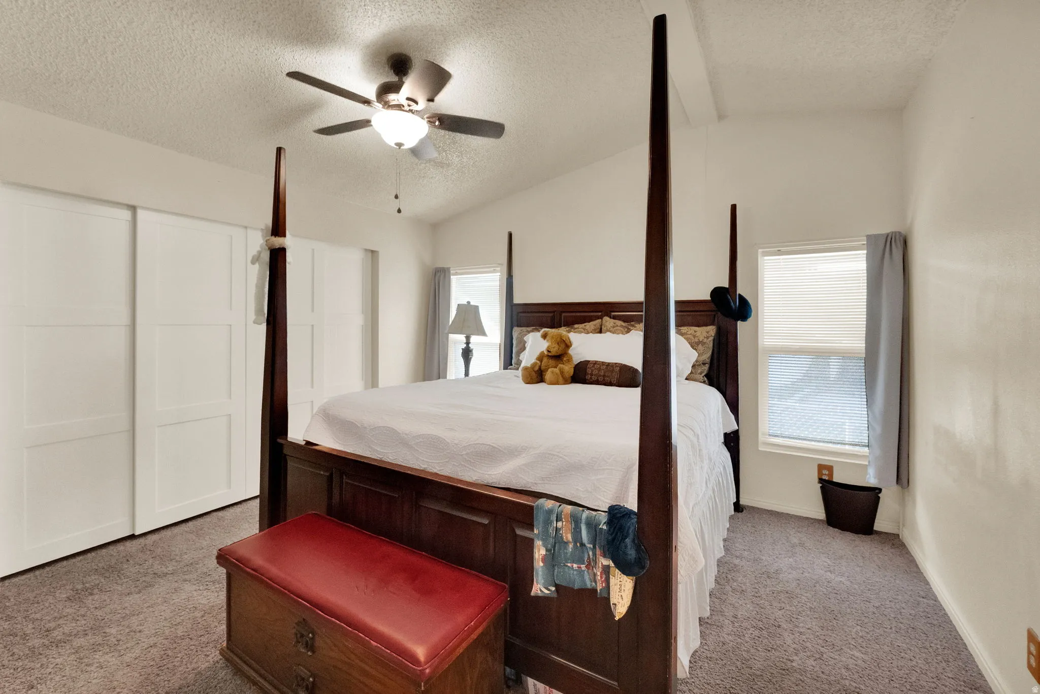 Bedroom with lofted ceiling, multiple windows, a textured ceiling, ceiling fan, and light colored carpet