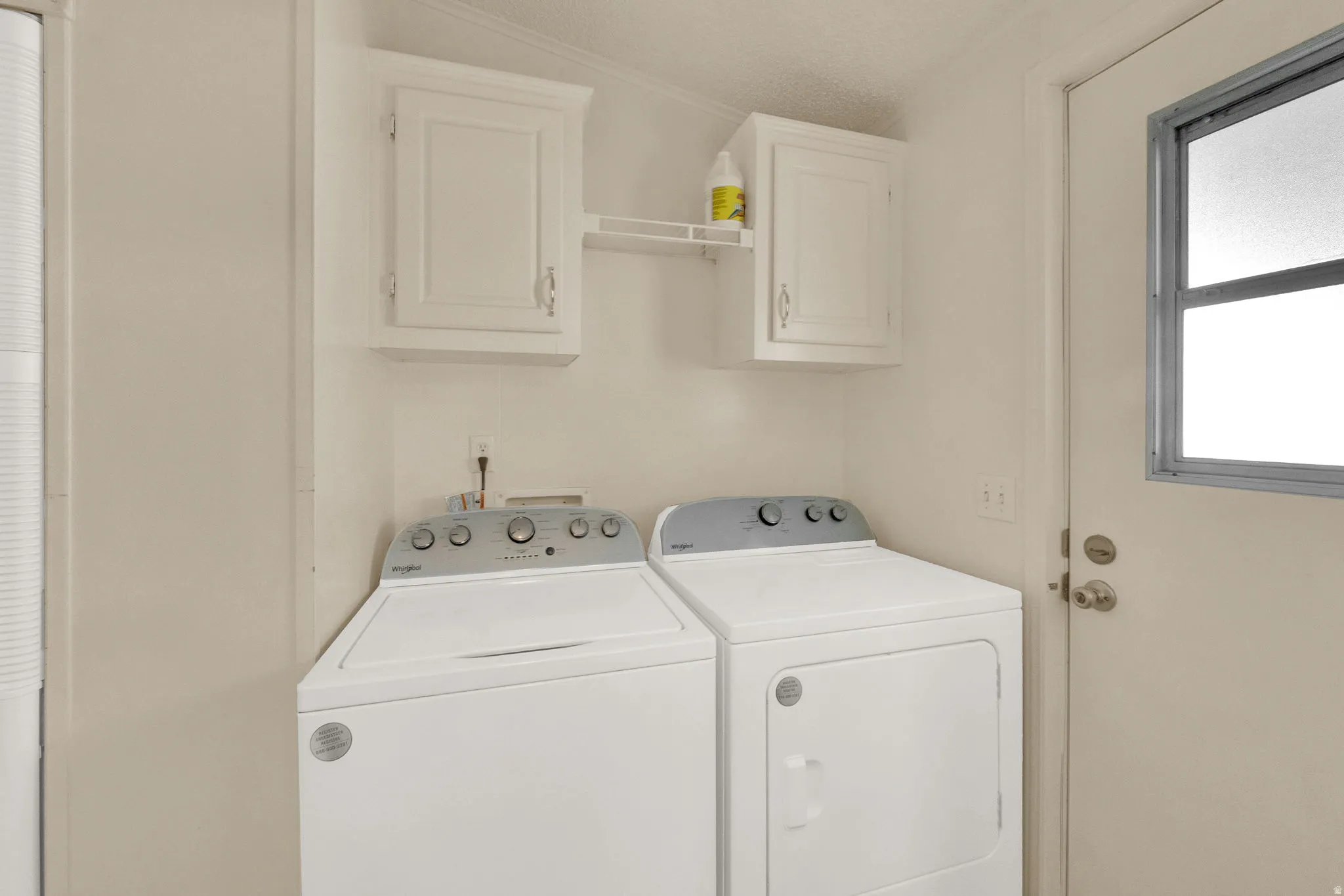 Washroom featuring independent washer and dryer, cabinet space, and a textured ceiling