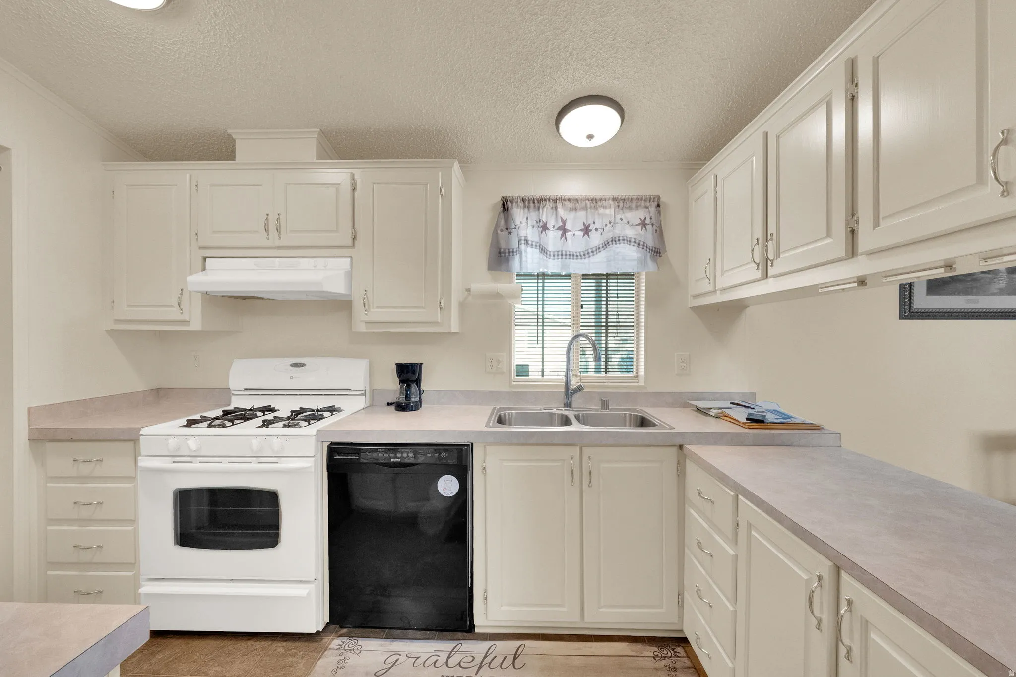 Kitchen featuring white gas range, a textured ceiling, dishwasher, light countertops, and ornamental molding