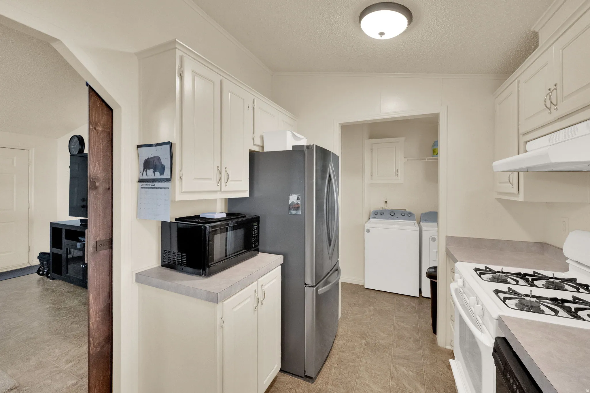 Kitchen featuring a textured ceiling, white gas range, white cabinets, black microwave, and light countertops