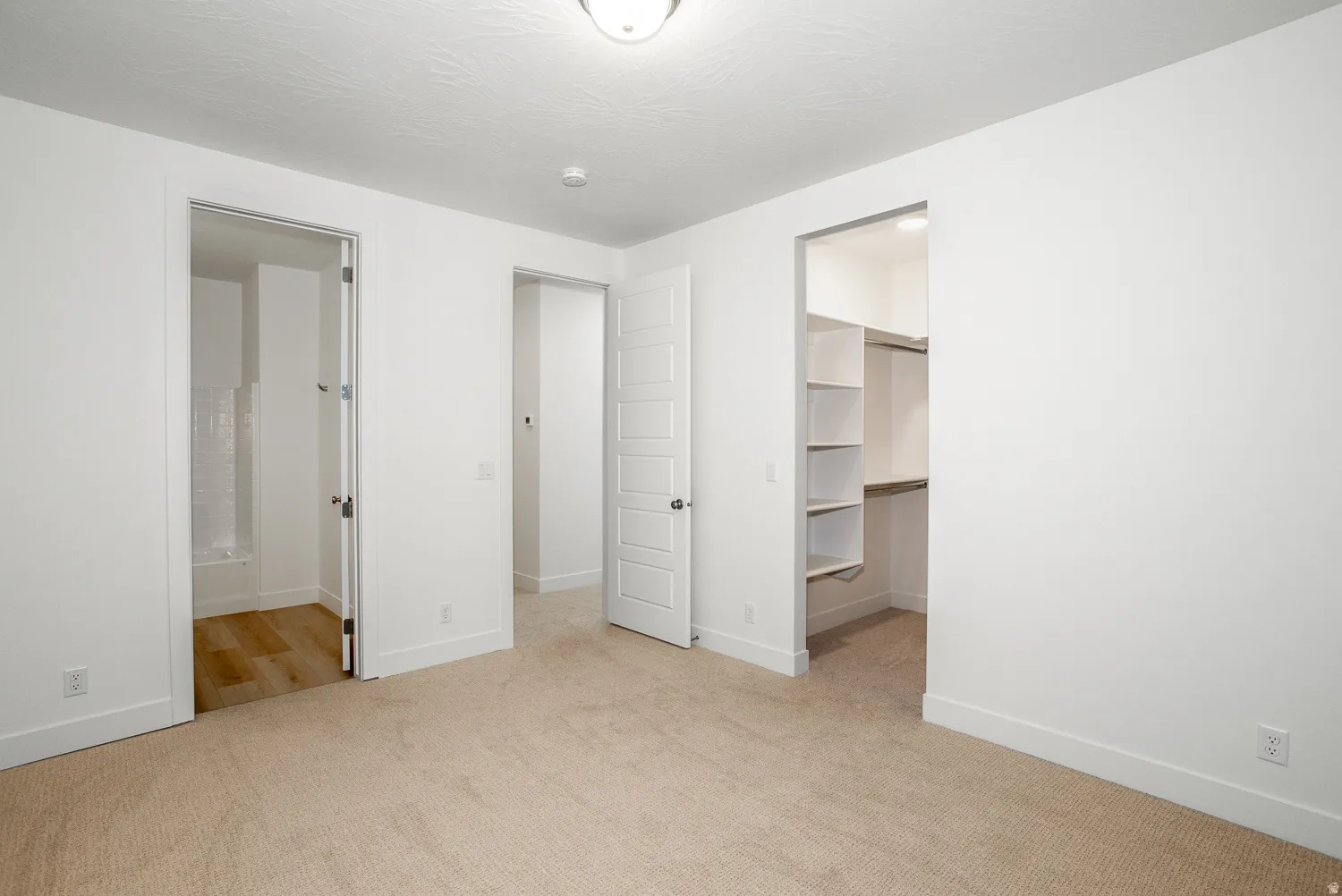 Unfurnished bedroom with light carpet, a spacious closet, and ensuite bath