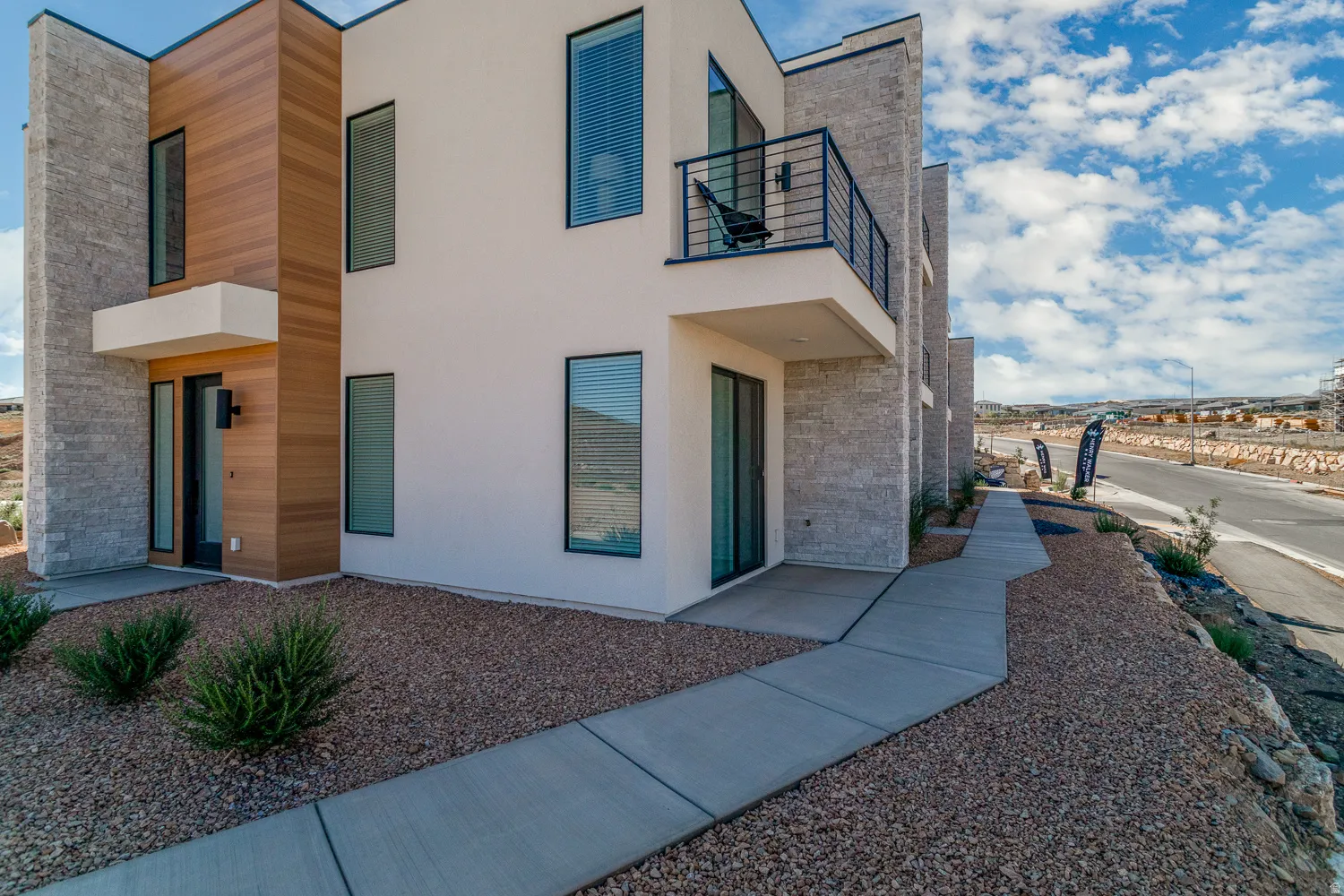 View of front facade featuring a balcony, stucco siding, and stone siding