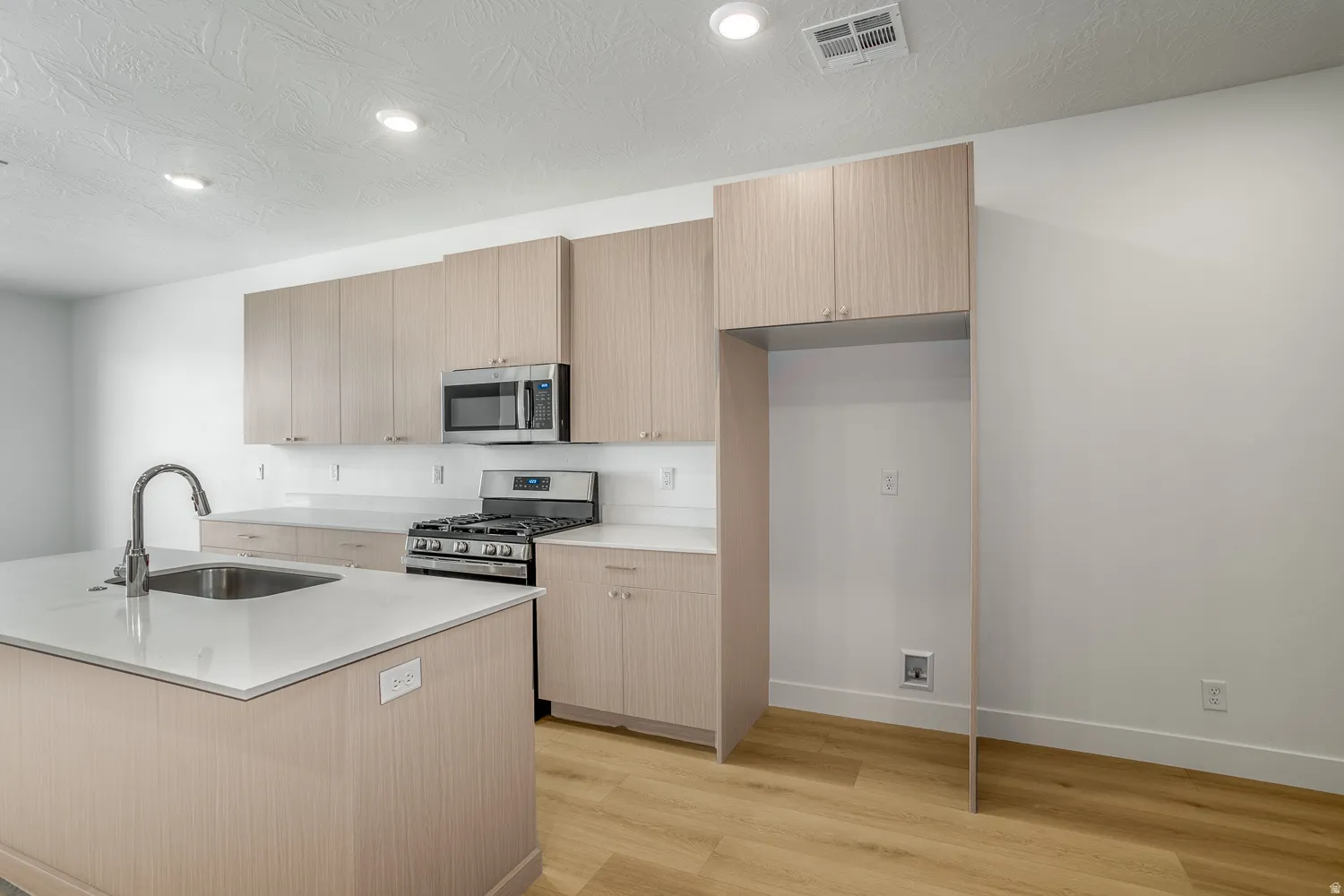 Kitchen featuring appliances with stainless steel finishes, modern cabinets, recessed lighting, light wood-type flooring, and light stone countertops