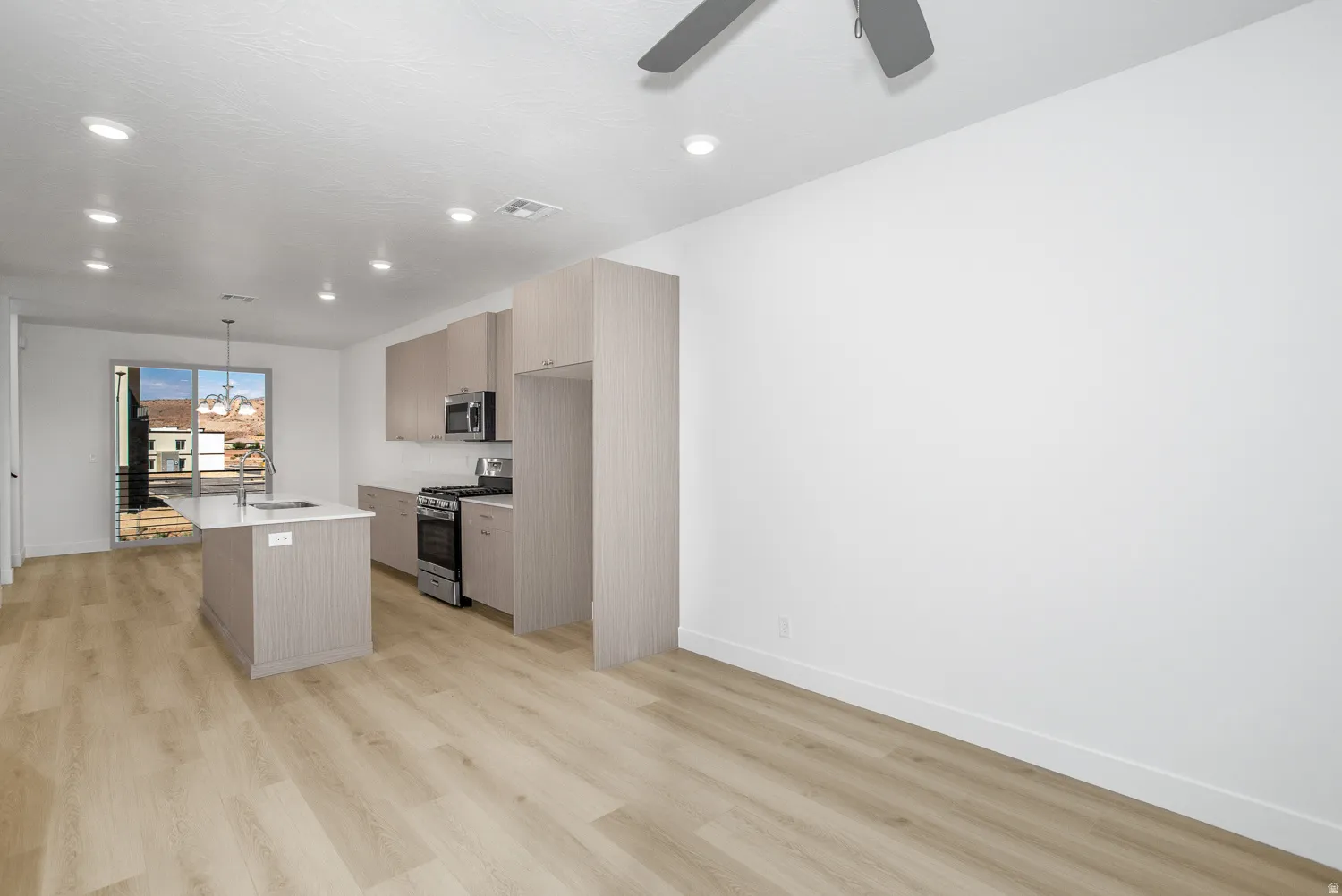 Kitchen with an island with sink, decorative light fixtures, appliances with stainless steel finishes, light wood-type flooring, and light brown cabinetry