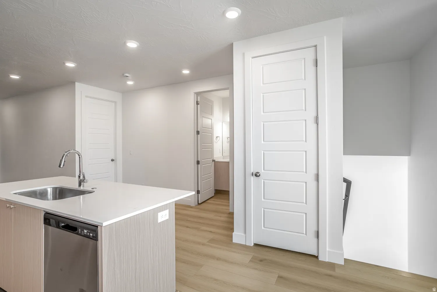 Kitchen featuring recessed lighting, dishwasher, a center island with sink, light wood-style flooring, and light stone counters