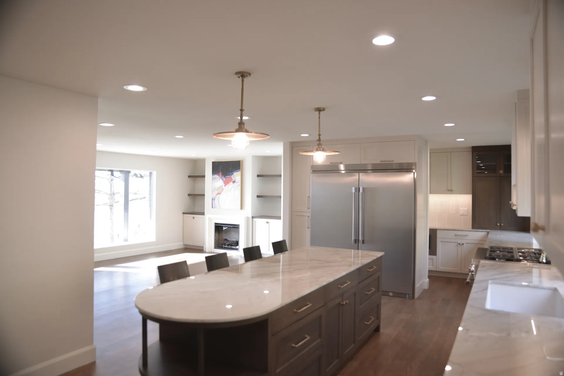 Kitchen featuring light stone countertops, appliances with stainless steel finishes, hanging light fixtures, a kitchen breakfast bar, and a glass covered fireplace