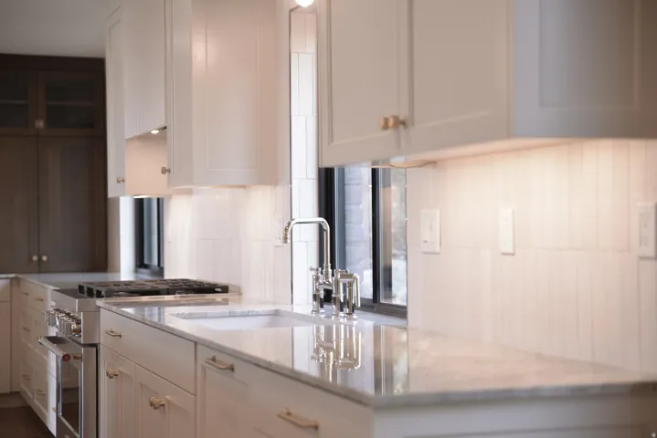 Kitchen with high end stove, decorative backsplash, light stone counters, and white cabinets