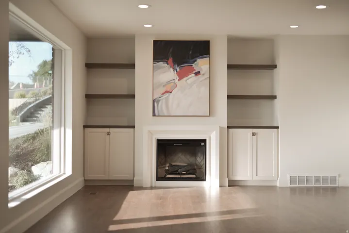 Unfurnished living room featuring built in shelves, a glass covered fireplace, recessed lighting, and dark wood-style flooring