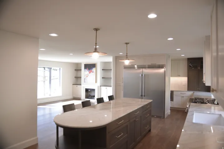 Kitchen featuring light stone countertops, appliances with stainless steel finishes, hanging light fixtures, a kitchen breakfast bar, and a glass covered fireplace