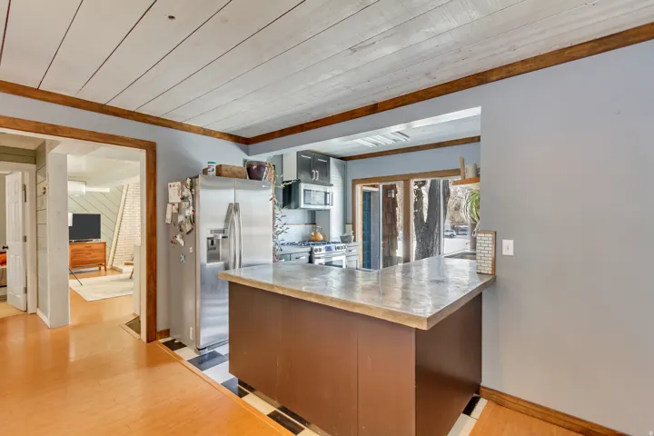 Kitchen featuring stainless steel appliances, a peninsula, light wood finished floors, light countertops, and wooden ceiling