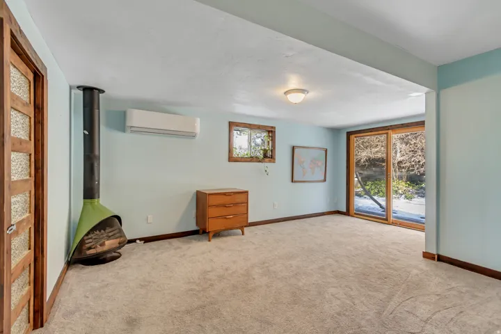 Carpeted spare room with a wood stove, plenty of natural light, and an AC wall unit