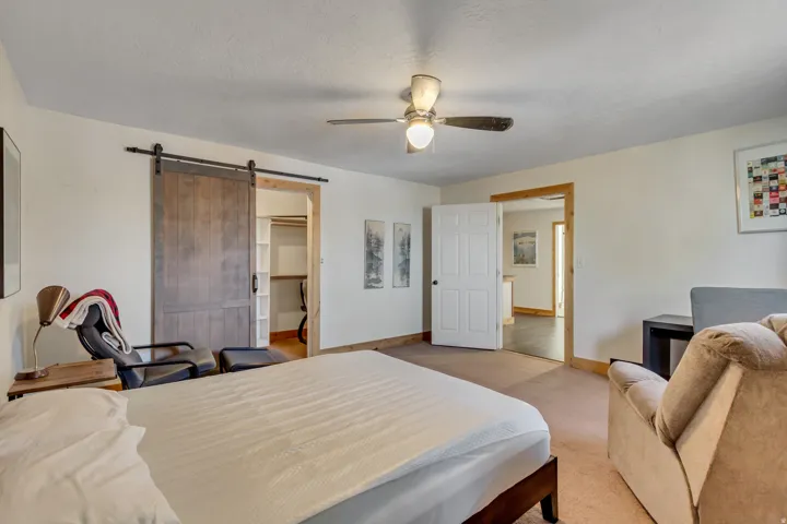 Carpeted bedroom with a barn door, a spacious closet, a ceiling fan, and a textured ceiling