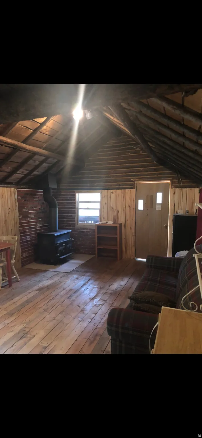 Living area featuring wooden walls, a wood stove, vaulted ceiling, and wood-type flooring