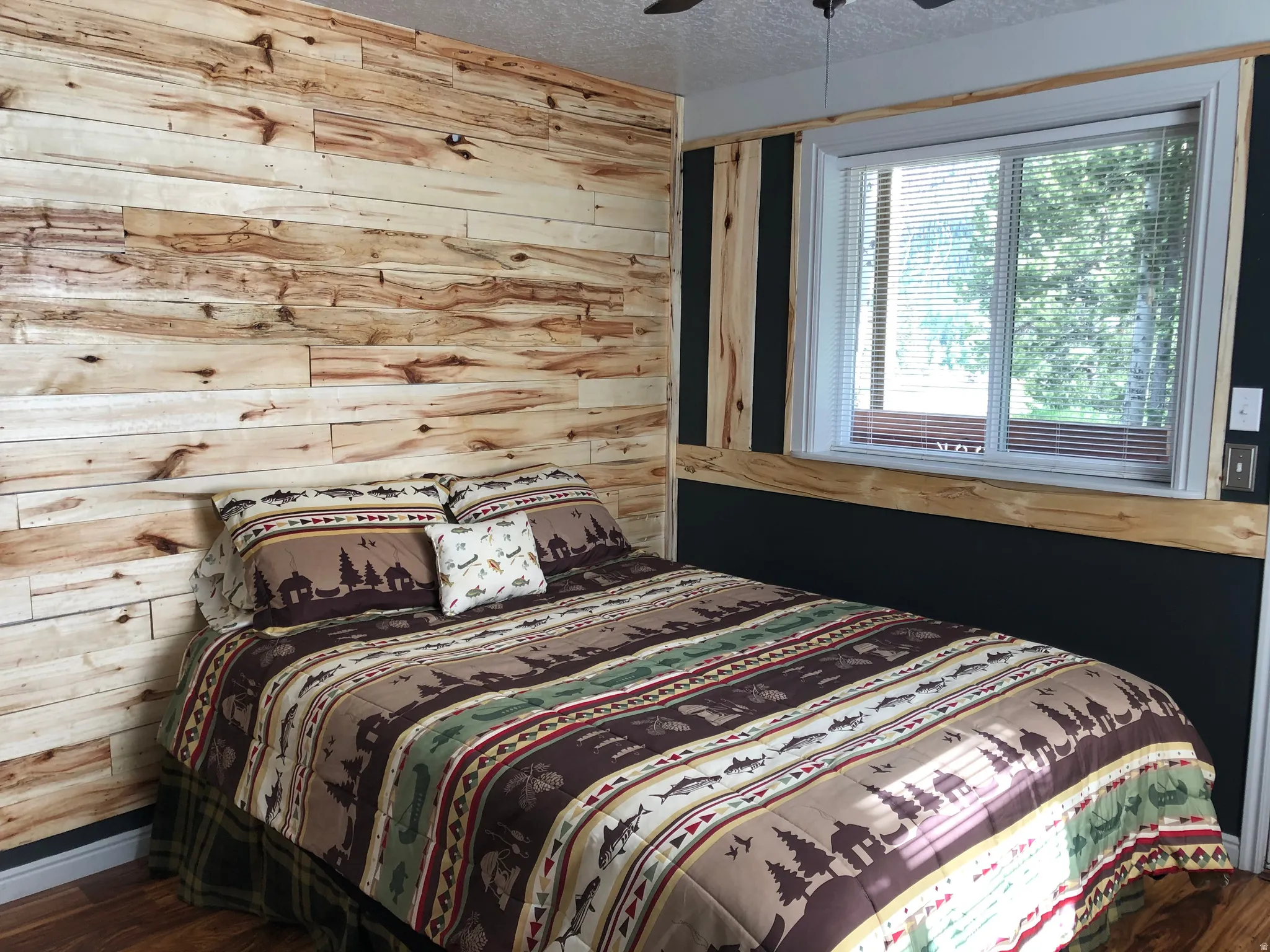 Bedroom featuring a textured ceiling, wooden walls, wood finished floors, and a ceiling fan