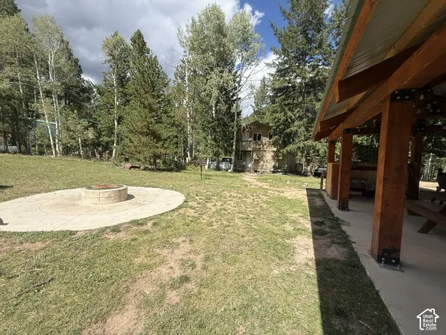 Spacious lawn area with a built-in fire pit on a concrete pad, complemented by a covered outdoor structure with exposed wood beams