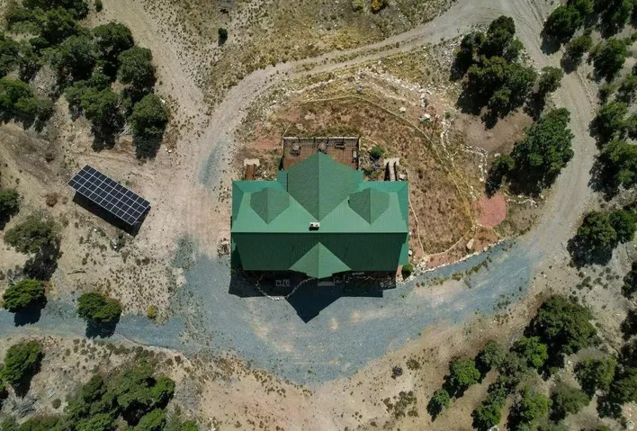 Gabled green roofline, gravel drive, surrounding natural vegetation, and solar panel array