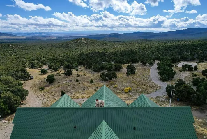 Expansive landscape featuring distant mountains, extensive natural foliage, a winding gravel path, and a structure with a green metal roof