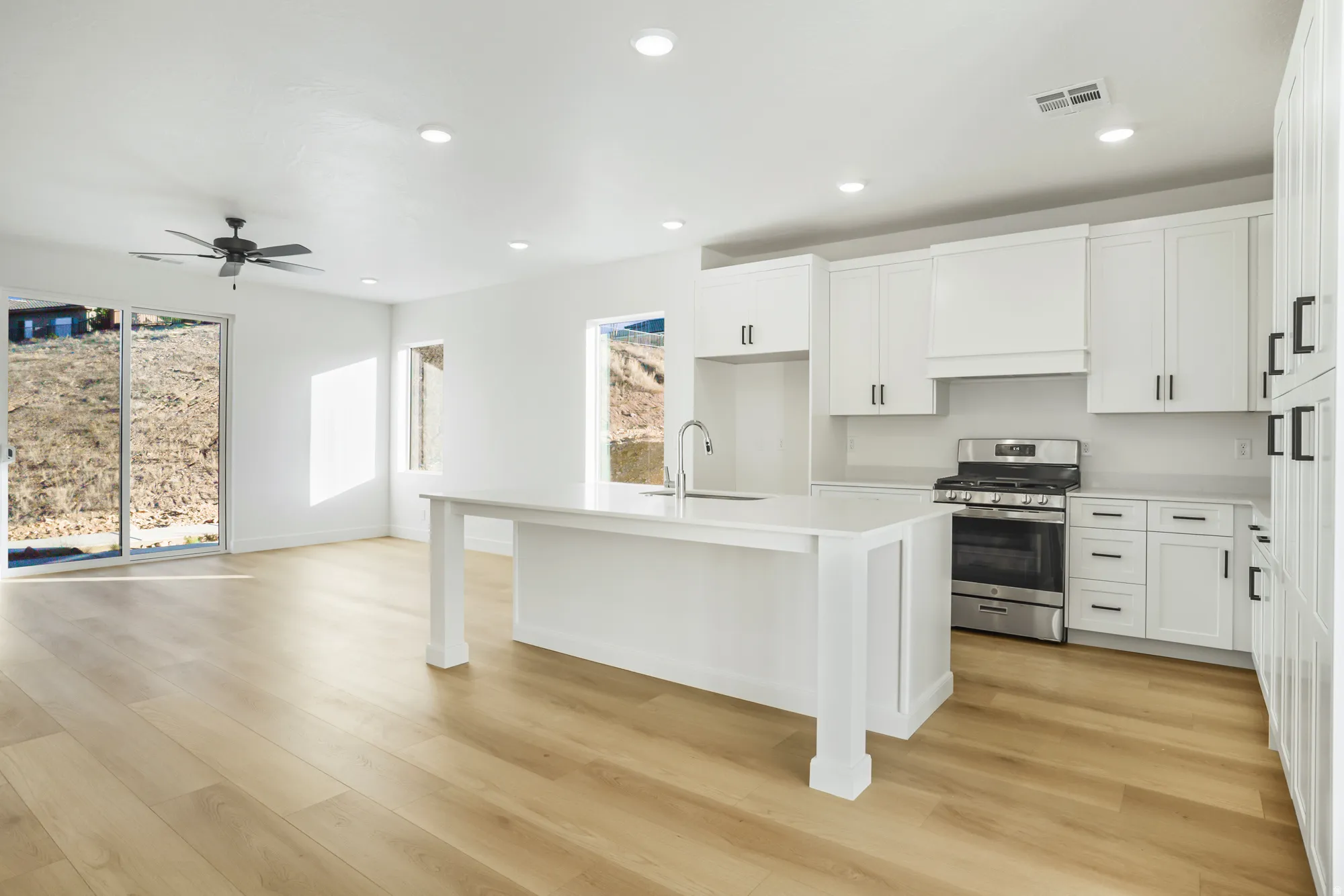 Open-concept kitchen and living area featuring light wood-finish flooring, white cabinetry, a central island with a sink, a stainless steel range, and recessed lighting