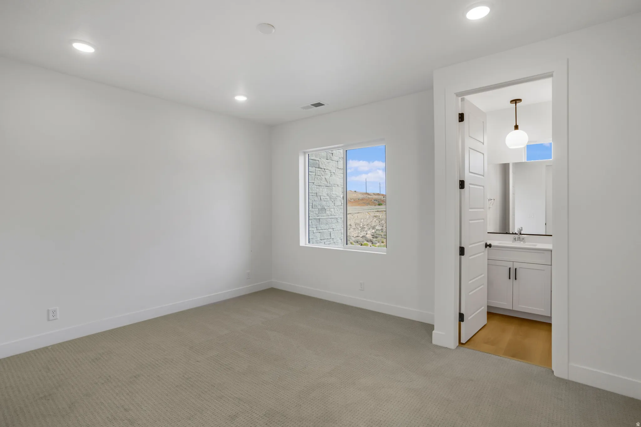 Neutral wall color with recessed lighting, light-toned carpeting, and a window with a stone exterior visible
