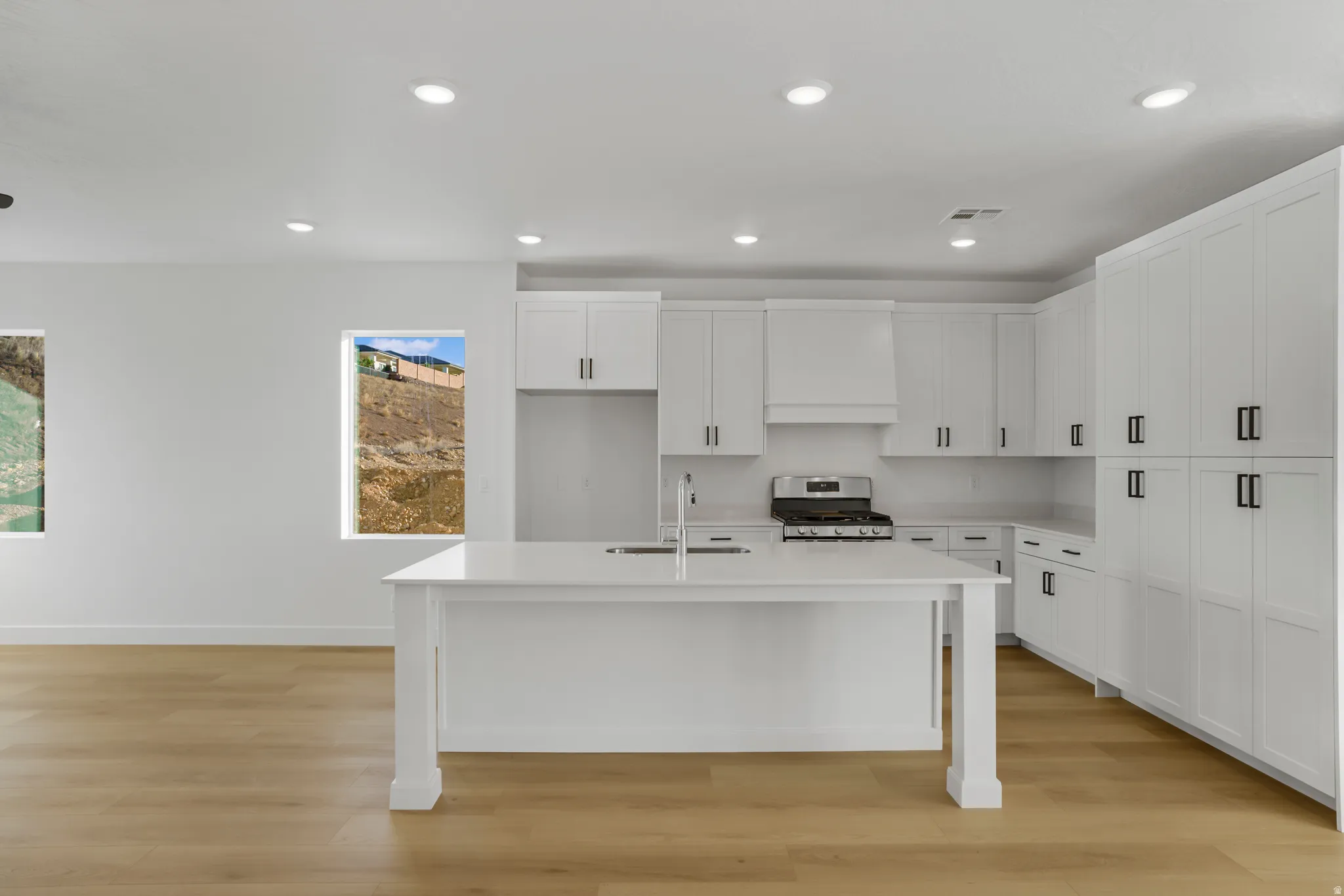 Modern kitchen featuring a large central island with an integrated sink, white cabinetry, stainless steel range, and light wood-finish flooring