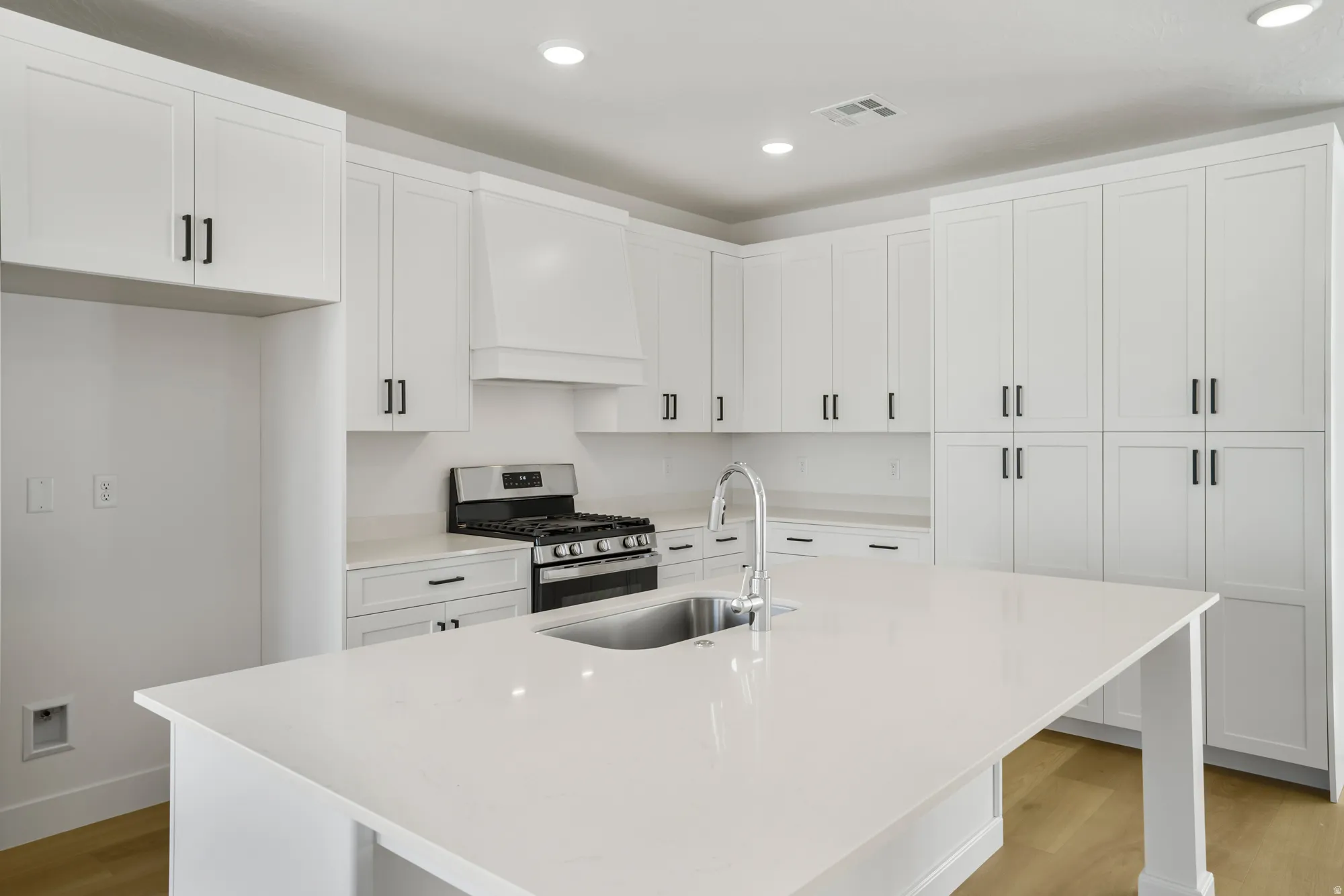 Kitchen featuring a central island with an undermount sink and gooseneck faucet, extensive white cabinetry with matte black hardware, light-toned countertops, and recessed lighting