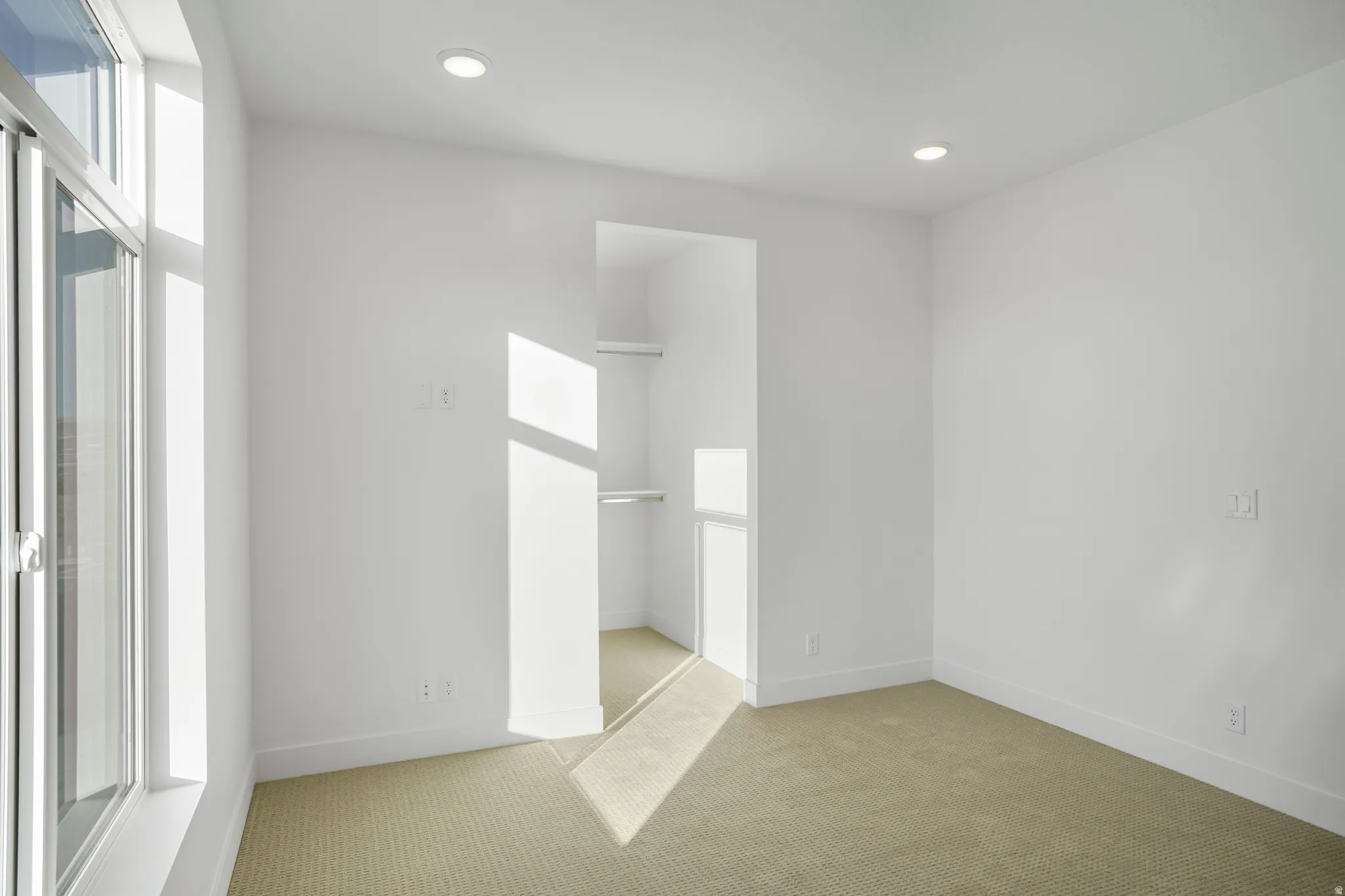Carpeted room featuring a large window, recessed lighting, and a built-in closet with shelving and hanging rods