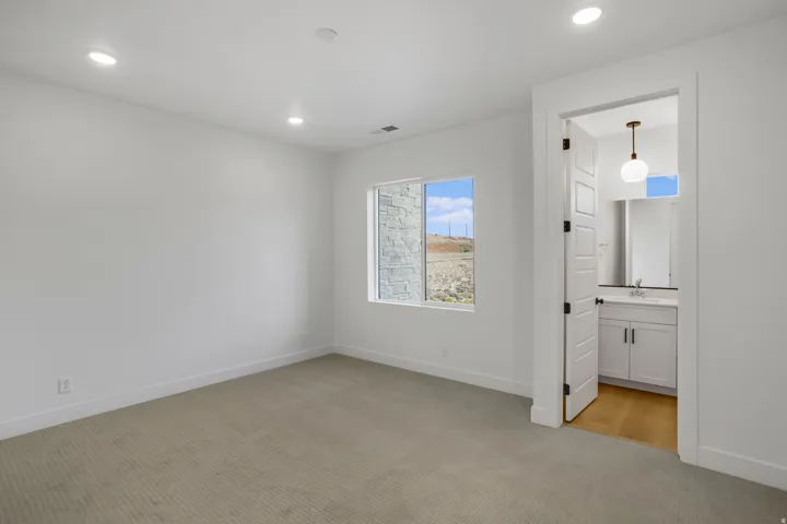 Neutral wall color with recessed lighting, light-toned carpeting, and a window with a stone exterior visible