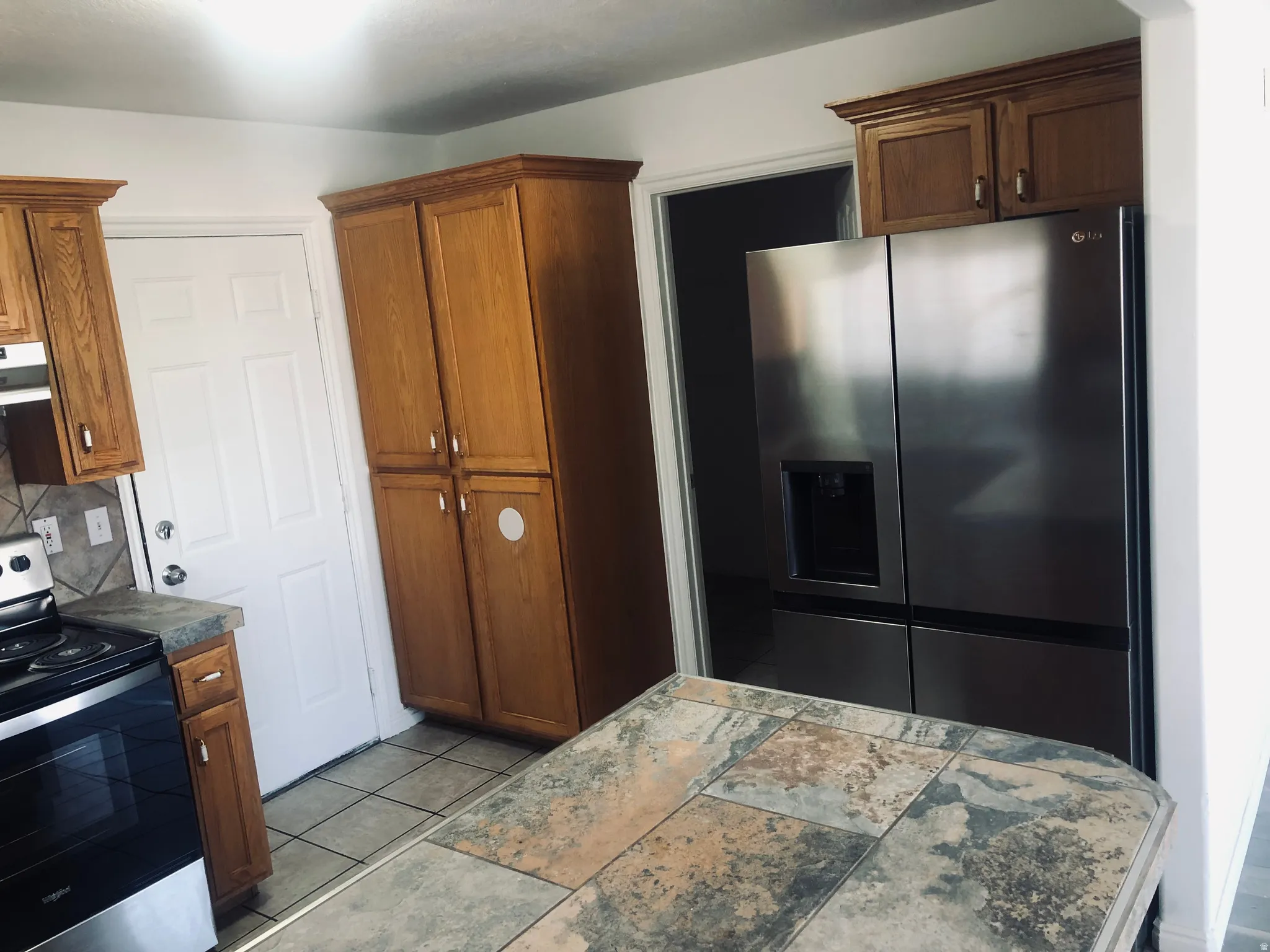 Kitchen with appliances with stainless steel finishes, brown cabinetry, under cabinet range hood, backsplash, and light tile patterned floors