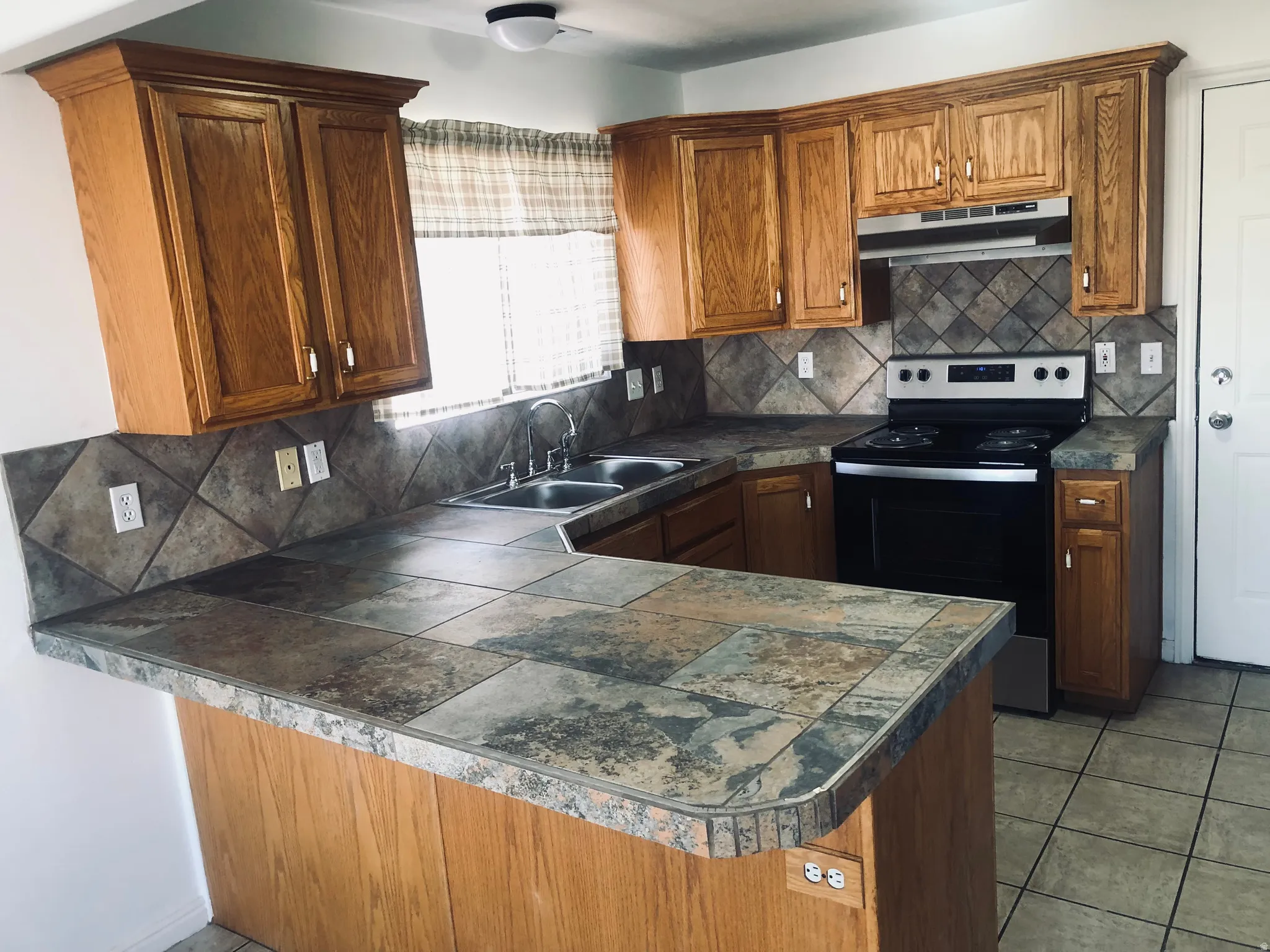 Kitchen featuring brown cabinets, tasteful backsplash, electric stove, and a peninsula