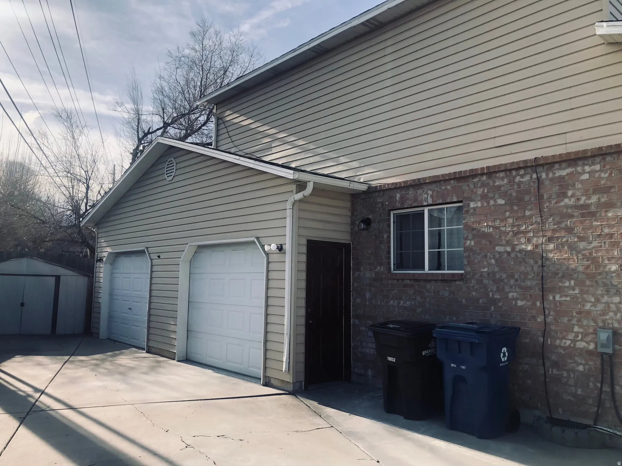 View of home's exterior with concrete driveway, brick siding, a storage unit, and an attached garage