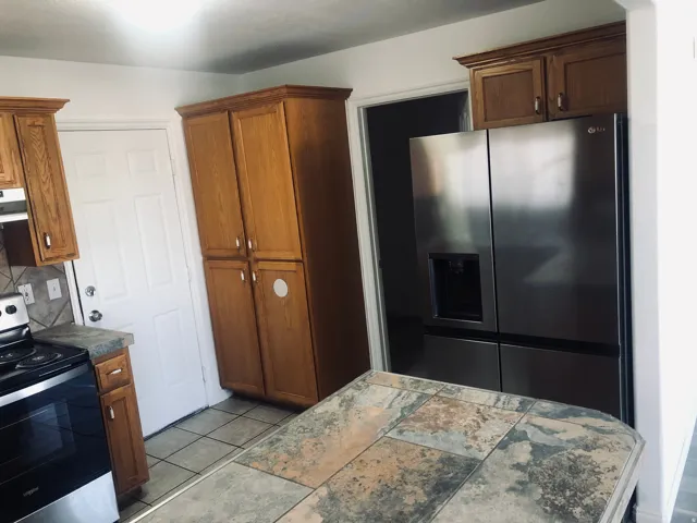 Kitchen with appliances with stainless steel finishes, brown cabinetry, under cabinet range hood, backsplash, and light tile patterned floors