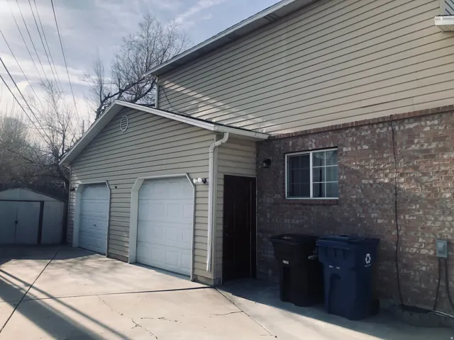 View of home's exterior with concrete driveway, brick siding, a storage unit, and an attached garage