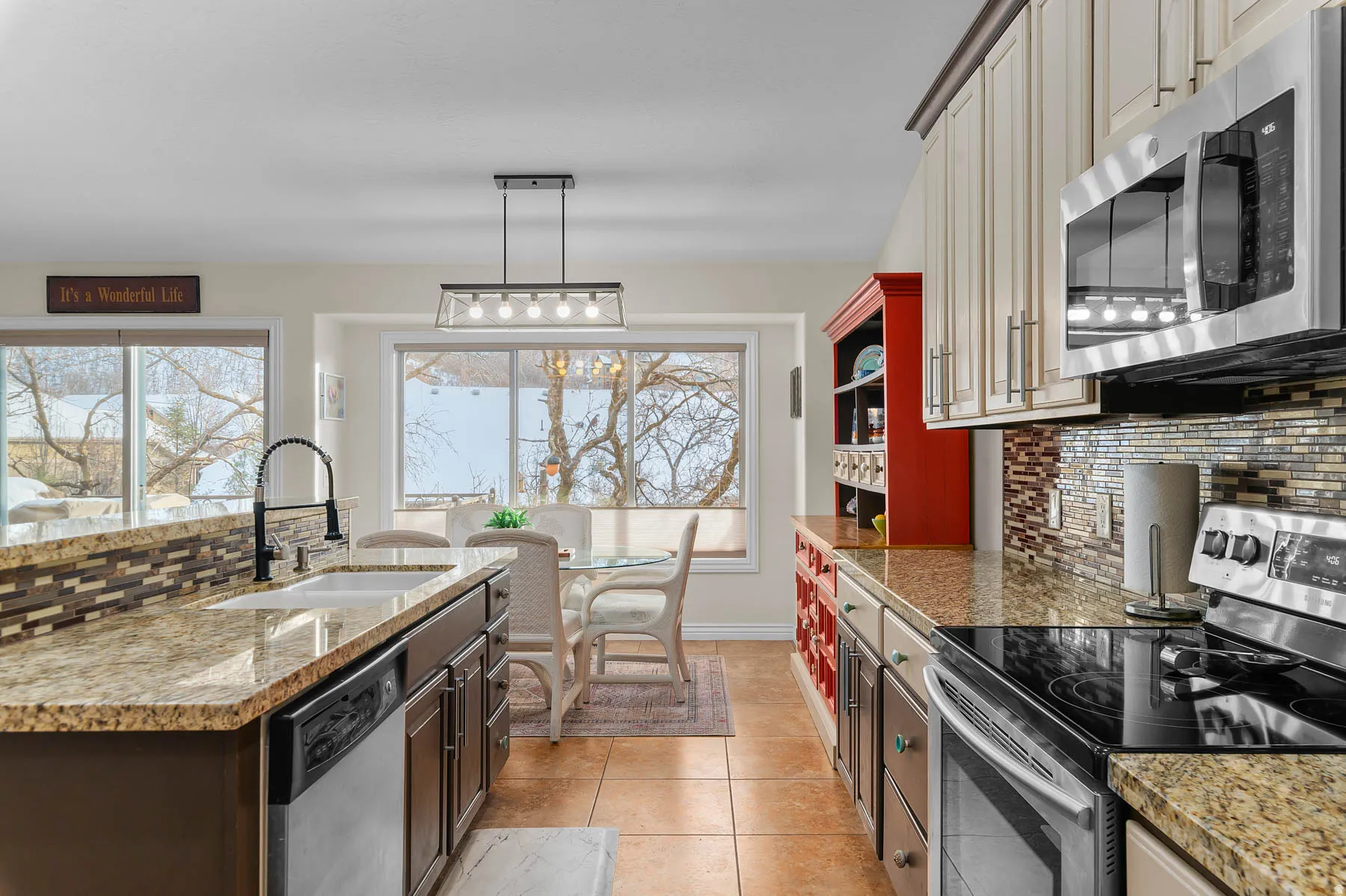 Kitchen featuring backsplash, stainless steel appliances, decorative light fixtures, light stone countertops, and light tile patterned floors
