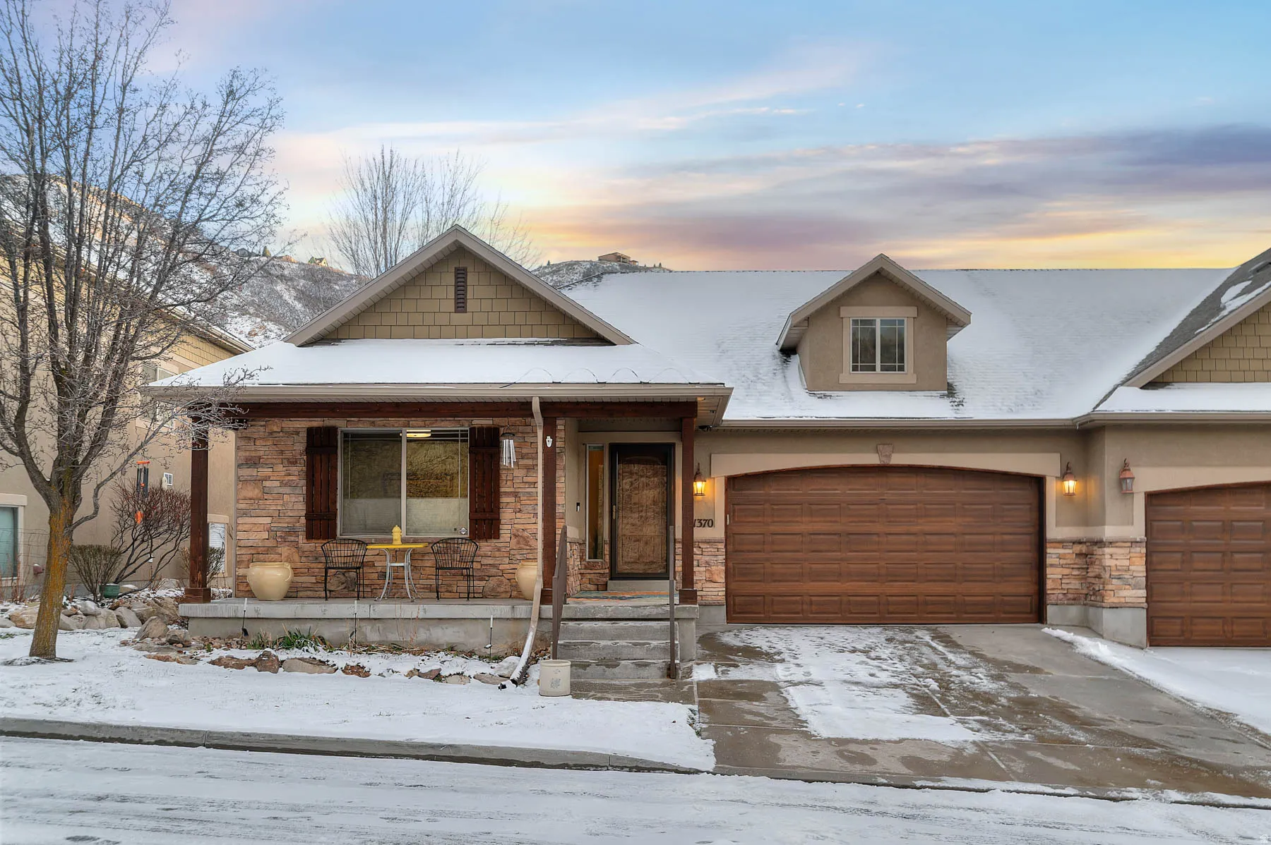 View of front of house featuring stone siding, covered porch, driveway, and an attached garage