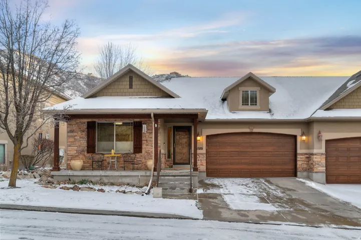 View of front of house featuring stone siding, covered porch, driveway, and an attached garage