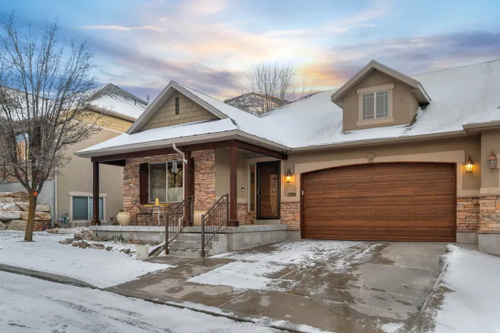 View of front of house featuring stone siding, driveway, stucco siding, and covered porch