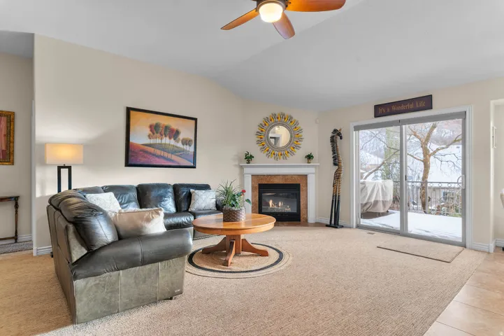 Living room with a fireplace with flush hearth, light carpet, lofted ceiling, ceiling fan, and light tile patterned flooring