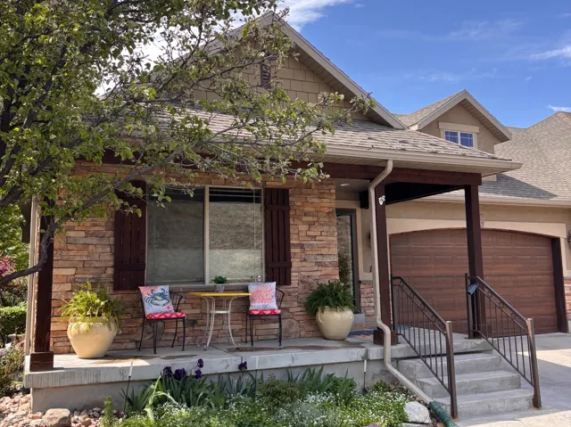 Stone facade home featuring a covered front porch, wood-look garage door, and detailed exterior shutters