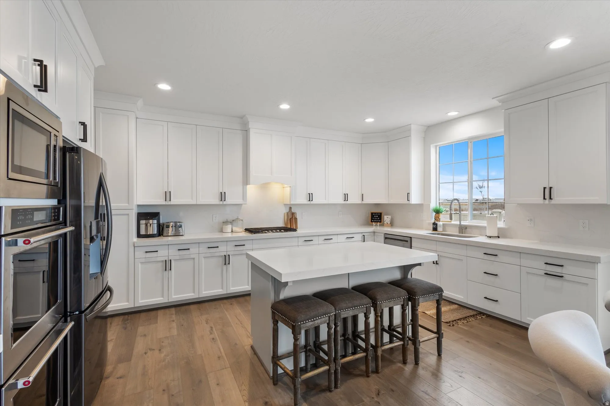 Kitchen with a kitchen breakfast bar, white cabinets, stainless steel appliances, light wood-type flooring, and a center island