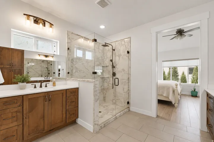 Walk-in shower with glass enclosure and marble-look tile, double vanity with wood-finish cabinetry, white countertop, and tiled flooring