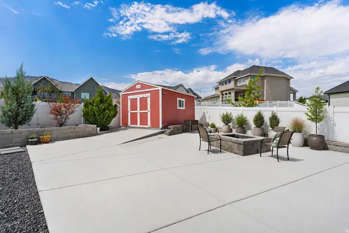 Expansive concrete patio with a built-in fire pit, privacy fencing, and a red storage shed