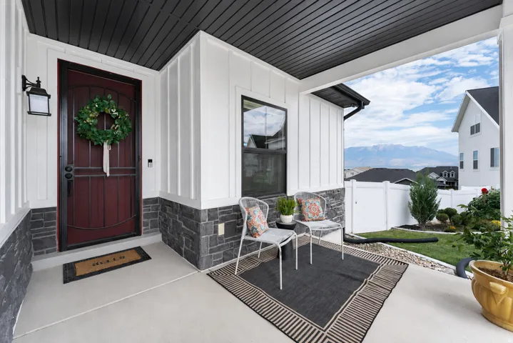 Covered front porch featuring board and batten siding with stone veneer, dark wood-finish entry door, and an exterior wall lantern